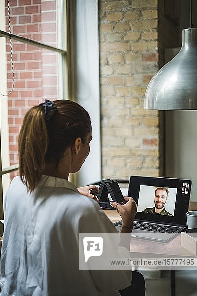 Rückansicht einer Designerin  die ein Modell in der Hand hält  während sie mit ihrem Kollegen per Videoanruf im Home-Office spricht