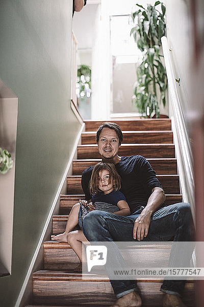 Porträt eines lächelnden Vaters mit Tochter  die zu Hause auf Stufen sitzen