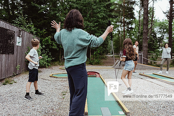 Rückansicht einer Frau  die mit ihrer Familie im Garten Minigolf spielt