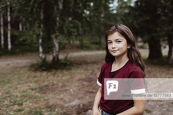 Porträt eines lächelnden Mädchens  das bei Bäumen im Wald steht