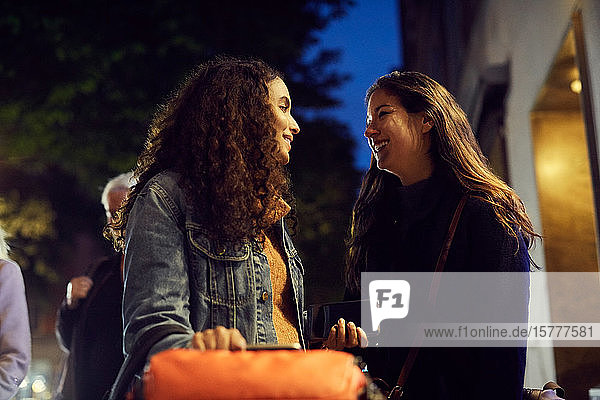 Smiling lesbian couple standing on sidewalk in city at night