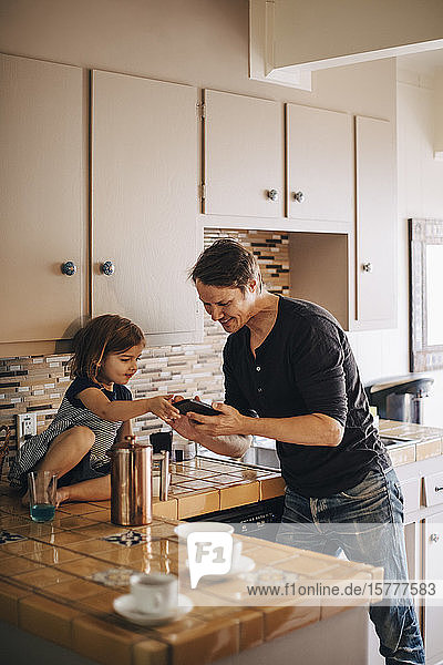 Vater zeigt der Tochter das Telefon  während er an der Küchentheke steht