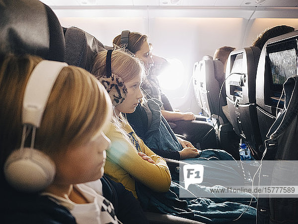 Seitenansicht von Mutter und Kindern  die im Flugzeug sitzen und Kopfhörer benutzen