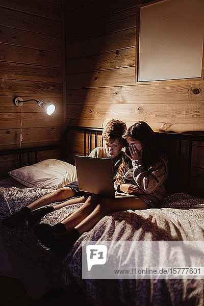 Geschwisterpaar benutzt Laptop in voller Länge  während es zu Hause auf dem Bett an der Wand sitzt