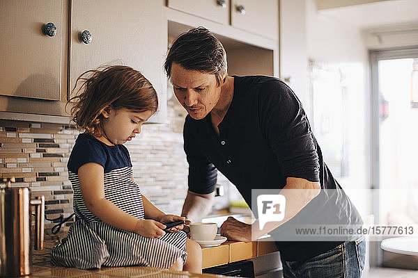Daughter using phone while father standing in domestic kitchen