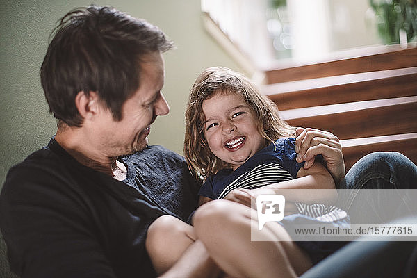 Portrait of happy daughter with smiling father sitting on steps at home