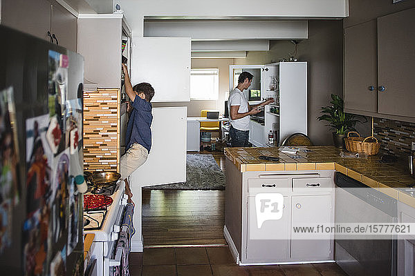 Junge hängt am Schrank  während der Vater zu Hause Glasgeschirr arrangiert