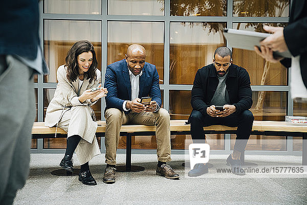 Unternehmer und Unternehmerinnen telefonieren  während sie an einem Bürogebäude sitzen