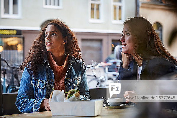 Lesbian couple looking while sitting at sidewalk cafe during weekend in city