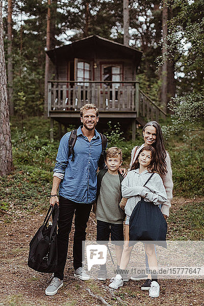 Ganzfigur einer Familie mit Gepäck  die im Wald vor einem Haus steht