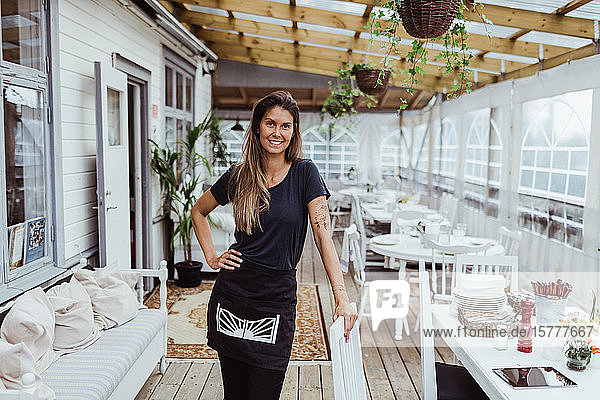 Portrait of smiling female owner standing by chair in restaurant