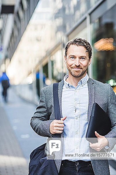 Porträt eines lächelnden reifen Unternehmers mit im Freien stehender Tasche
