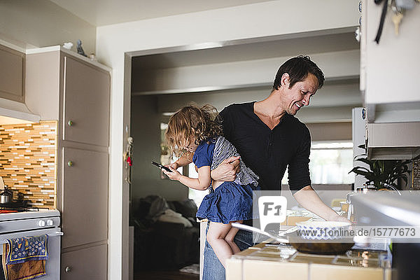 Tochter telefoniert  während der Vater lächelnd in der Küche arbeitet