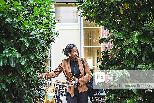 Lächelnde Architektin schaut weg  während sie mit dem Fahrrad am Haus steht