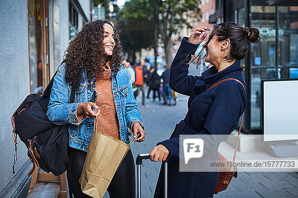 Lächelnde Frau steht mit Freundin auf dem Bürgersteig in der Stadt während des Urlaubs