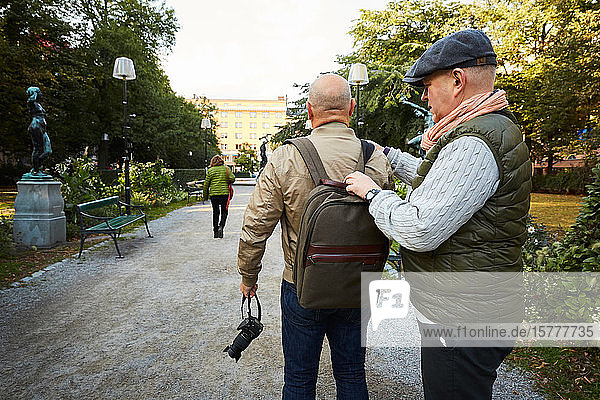 Senior man adjusting bag strap of friend while standing at park in city