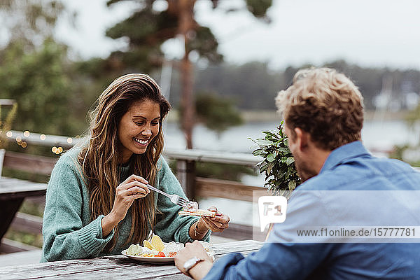 Smiling woman eating food while sitting with male friend in restaurant