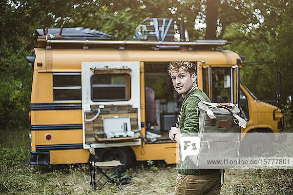 Rückansicht Porträt eines Mannes mit Rucksack auf dem Weg zum Wohnmobil im Wald beim Camping
