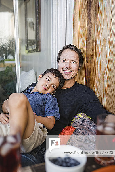 Porträt eines lächelnden Vaters mit Sohn an einer Holzwand sitzend