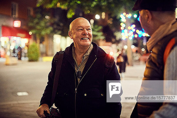 Smiling senior man looking at male friend while standing on street in city at night