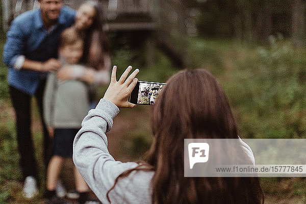 Mädchen fotografiert Familie mit Mobiltelefon  während sie im Hinterhof steht