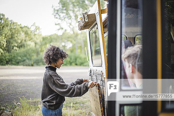 Side view of smiling woman adjusting wood on caravan door during camping in forest