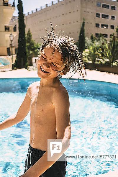 Lächelnder Junge ohne Hemd  der sich am Swimmingpool des Ferienorts vergnügt