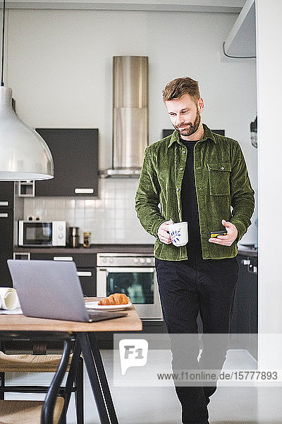 Male architect with coffee cup walking by table at home