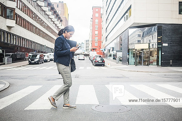 Geschäftsfrau benutzt Mobiltelefon beim Überqueren einer Straße