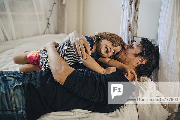 Mature father kissing daughter while lying on bed