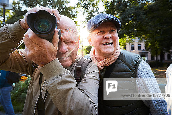 Senior man using camera while standing with friend at park in city