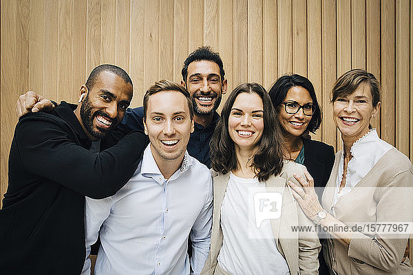 Porträt von glücklichen Unternehmerinnen und Unternehmern  die an einer Holzwand stehen