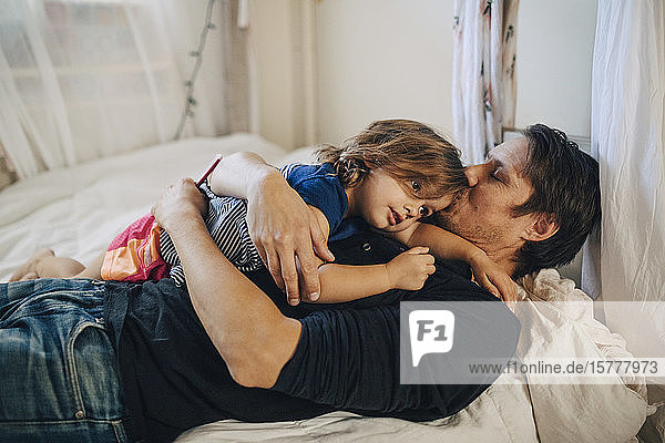 Mature father with eyes closed kissing daughter while lying on bed