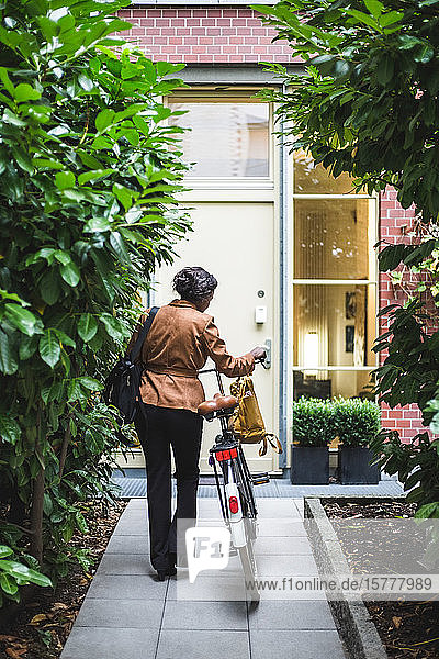 Rückansicht einer Architektin mit Fahrrad am Haus stehend