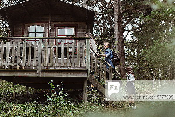 Familie mit Gepäck geht im Urlaub auf der Treppe eines Hauses im Wald