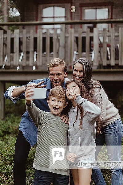 Smiling boy taking selfie with family on mobile phone while standing against house