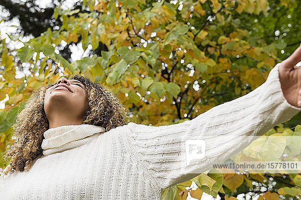 Smiling woman with her arms outstretched by tree
