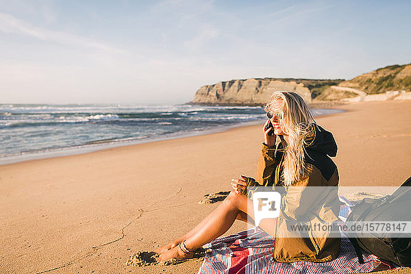 Smiling woman talking on phone sitting on beach