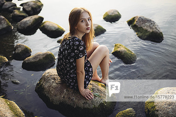 Frau in schwarzem Kleid sitzt auf einem Felsen im Meer