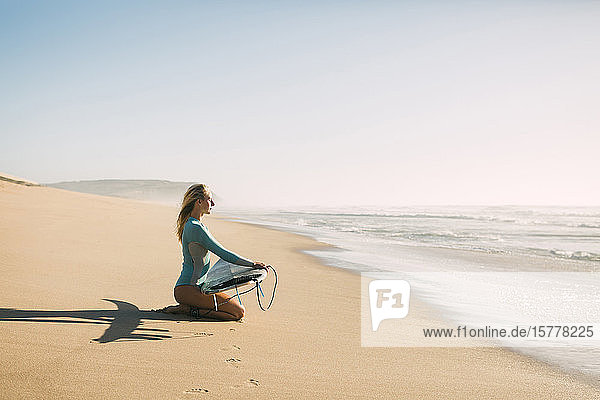 Frau kniend mit Surfbrett am Strand