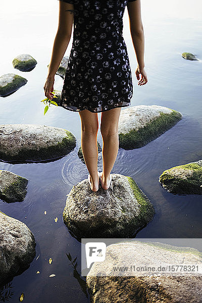Barfüßige Frau steht auf einem Felsen im Meer