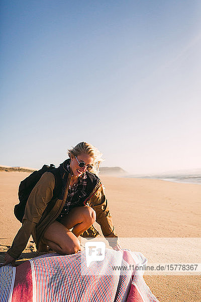 Lächelnde Frau  die ihr Handtuch am Strand ablegt
