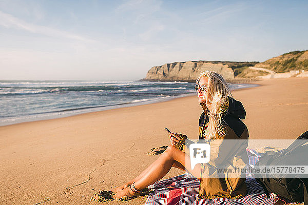 Frau hält Telefon am Strand sitzend