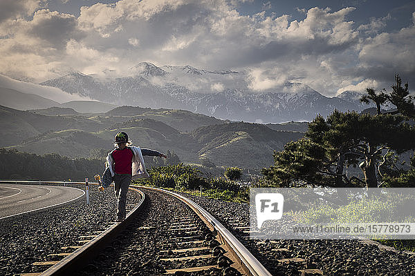 Junge  der entlang einer Eisenbahnlinie geht und ein Skateboard hält  Kaikoura  Gisborne  Neuseeland
