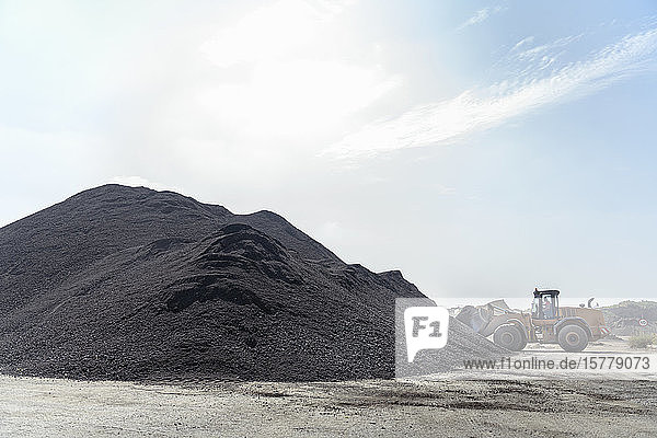 Digger with large pile of recycled soil in concrete recycling site
