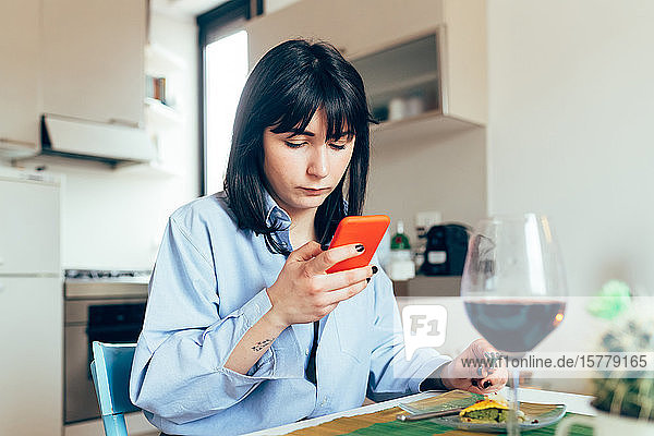 Frau sitzt am Tisch und schreibt SMS mit Mobiltelefon