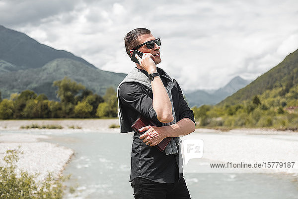 Geschäftsmann am Flussufer eines Gebirgsflusses telefoniert mit einem Smartphone  Francenigo  Venetien  Italien