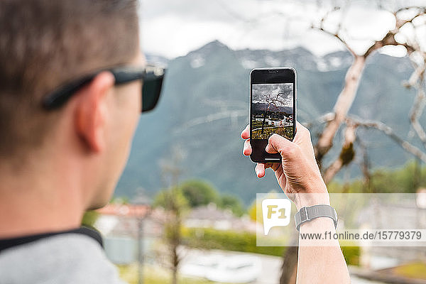 Male tourist taking smartphone photograph of mountain village over shoulder view Francenigo Veneto Italy