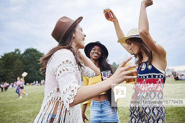 Friends drinking and dancing with arms raised in music festival