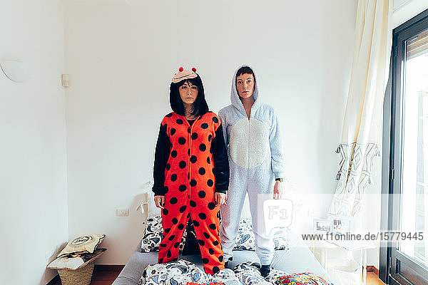 Portrait of women wearing adult bodysuit standing on bed looking at camera